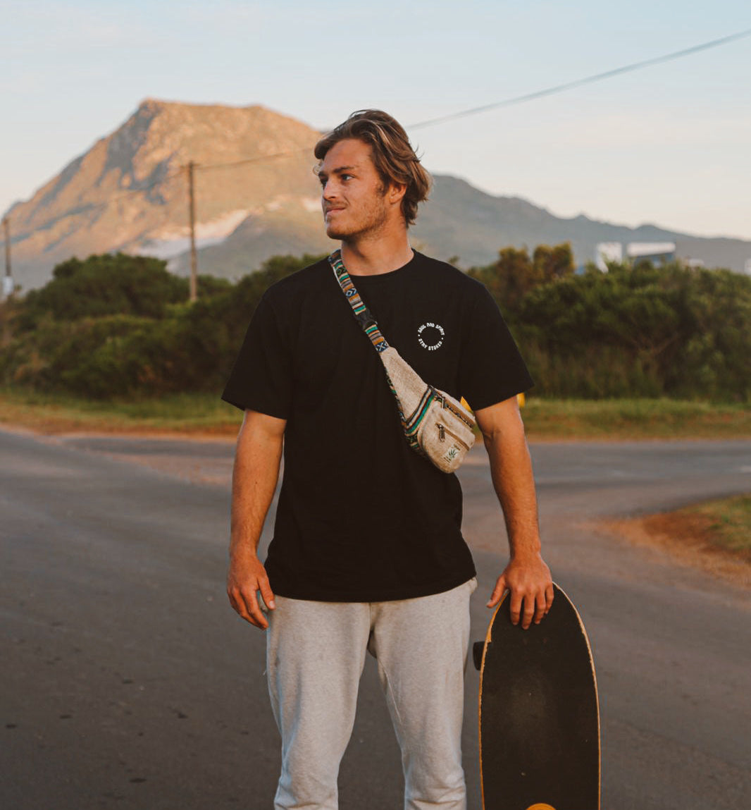 Man holding a skateboard on a road with mountains in the background