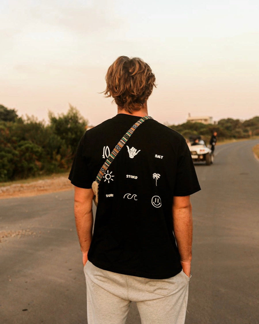 Person wearing a black t-shirt with white graphics on a road at sunset