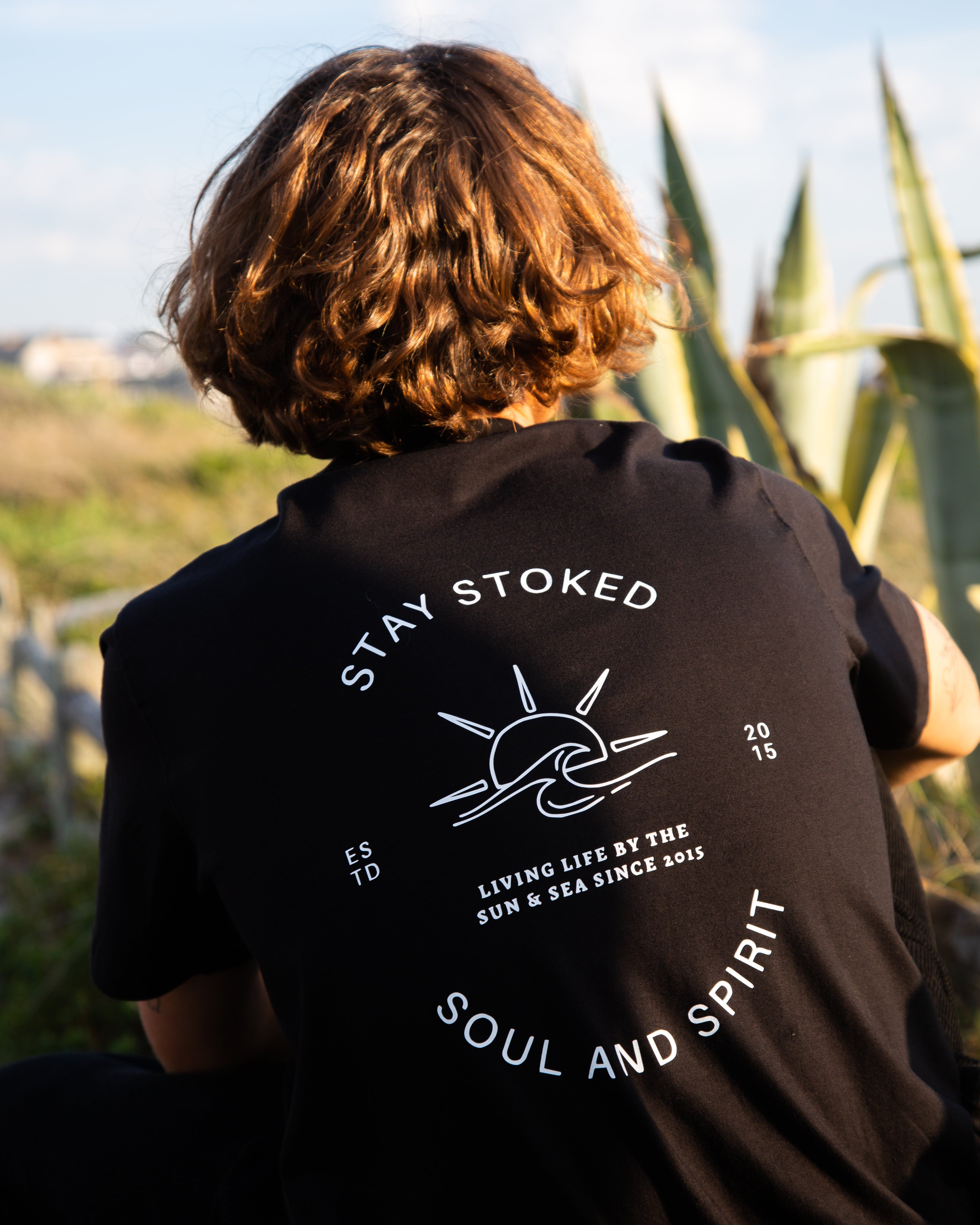Person wearing a black t-shirt with 'Stay Stoked' text and graphics outdoors.