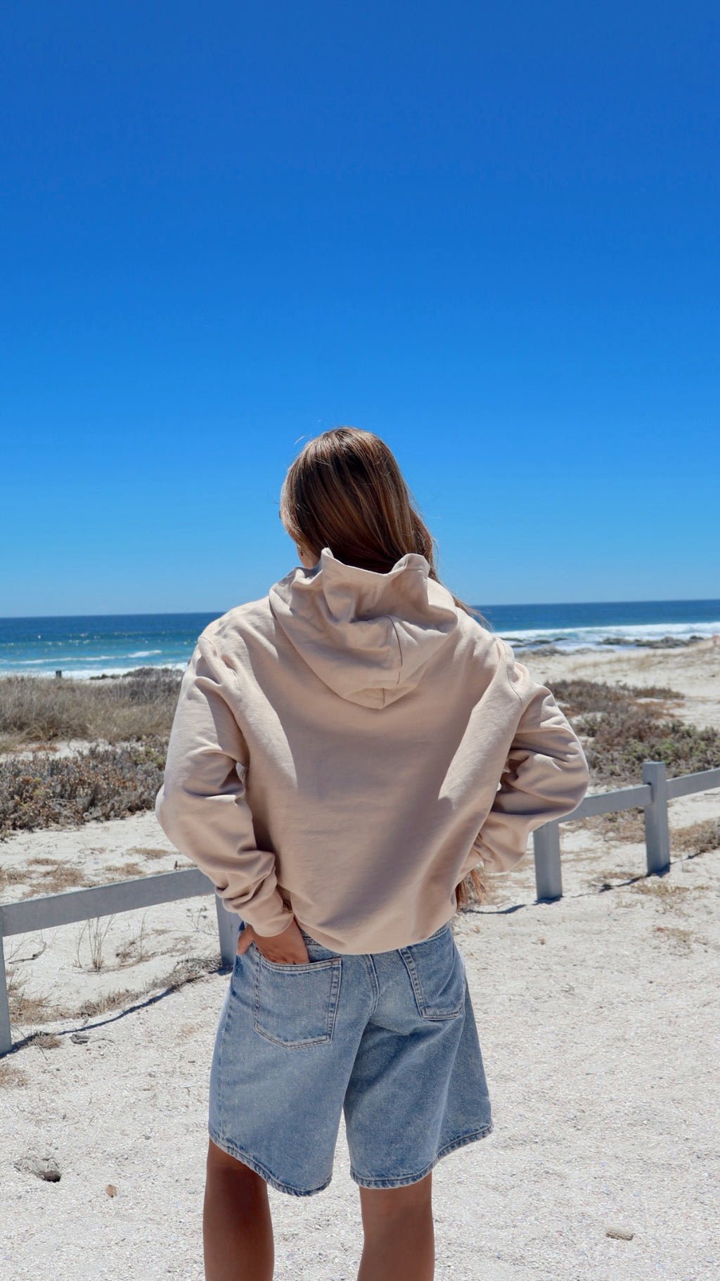 Beige pacific hoodie back view with ocean in background.
