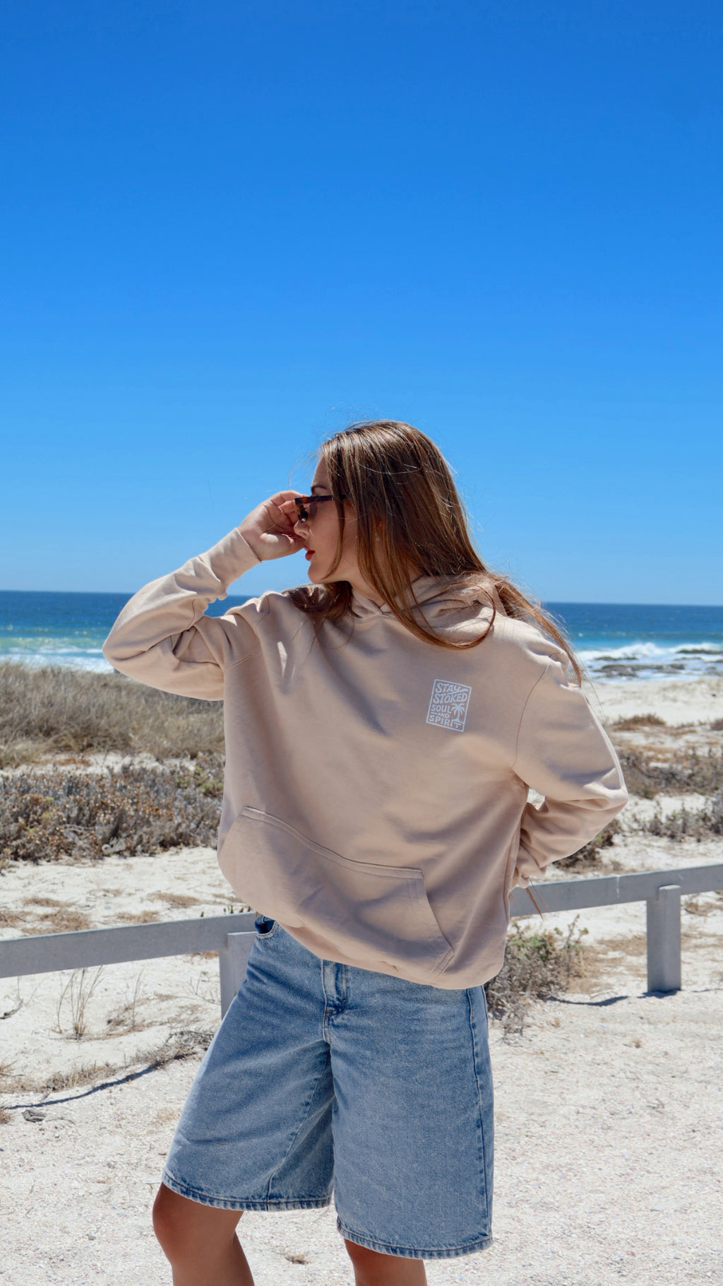 Beige pacific hoodie front view with ocean in background.
