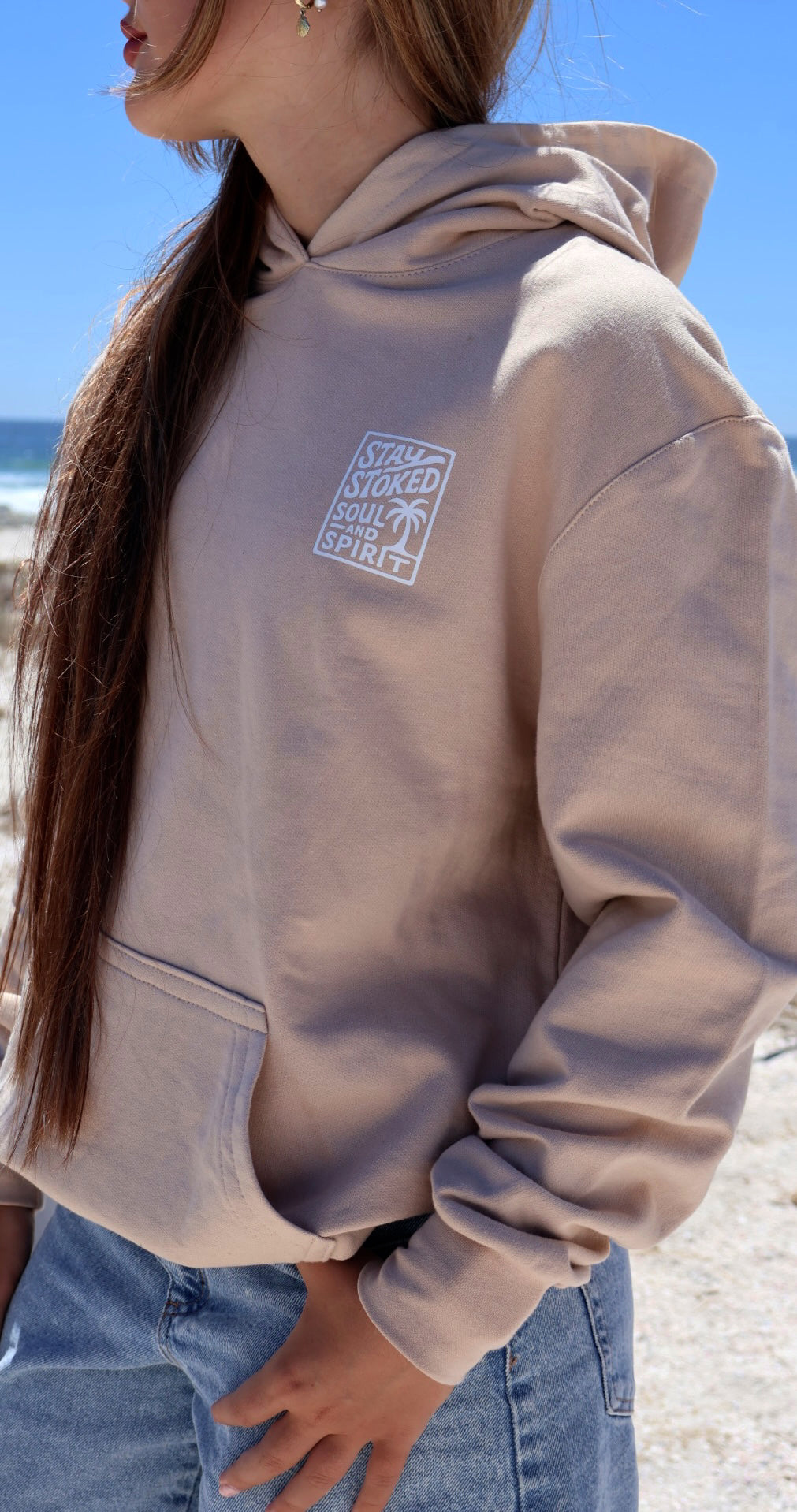 Beige pacific hoodie front view with ocean in background.